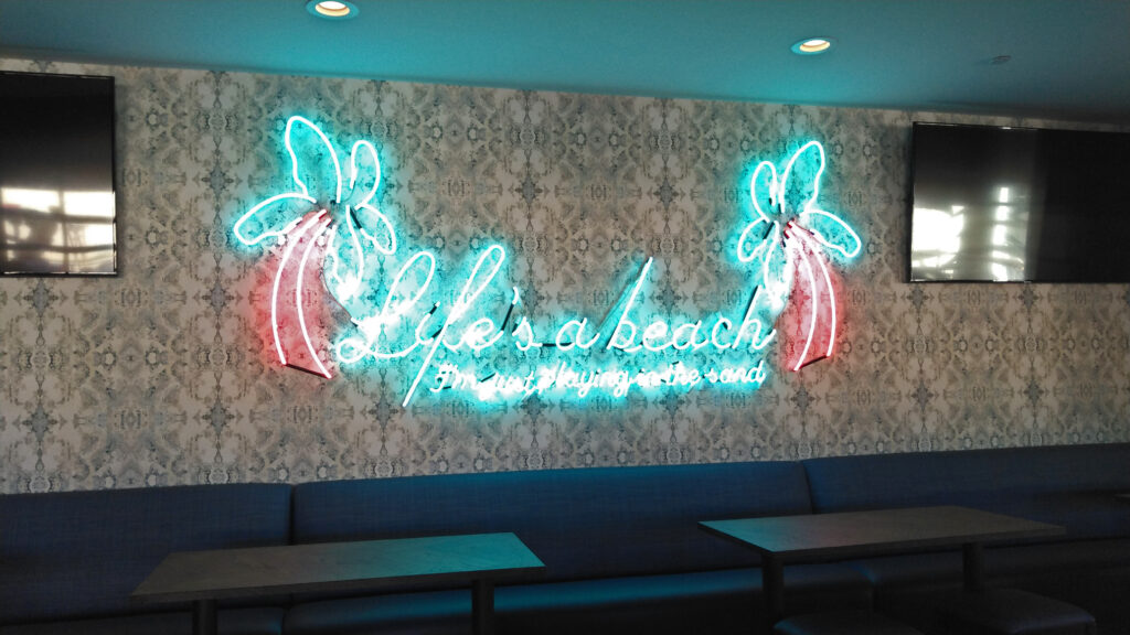 Neon Houston wall signs from Drift Bar that reads "Life's a beach I'm just playing in the sand"
