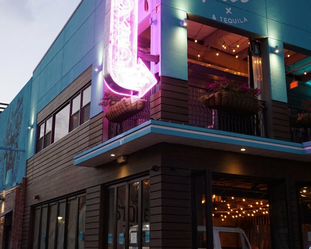 A tall pink neon blade sign glowing over the Stoked Tacos storefront at dusk, built by 4D SignWorx in Houston