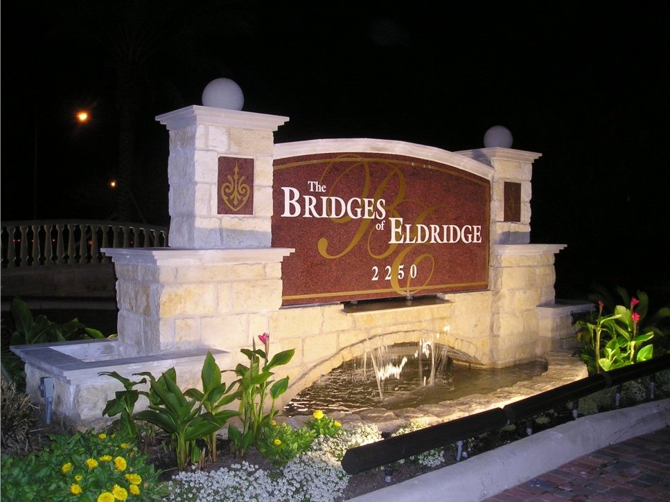 The Bridges of Eldridge entrance monument lit at night above a water cascade, built by 4D SignWorx in Houston