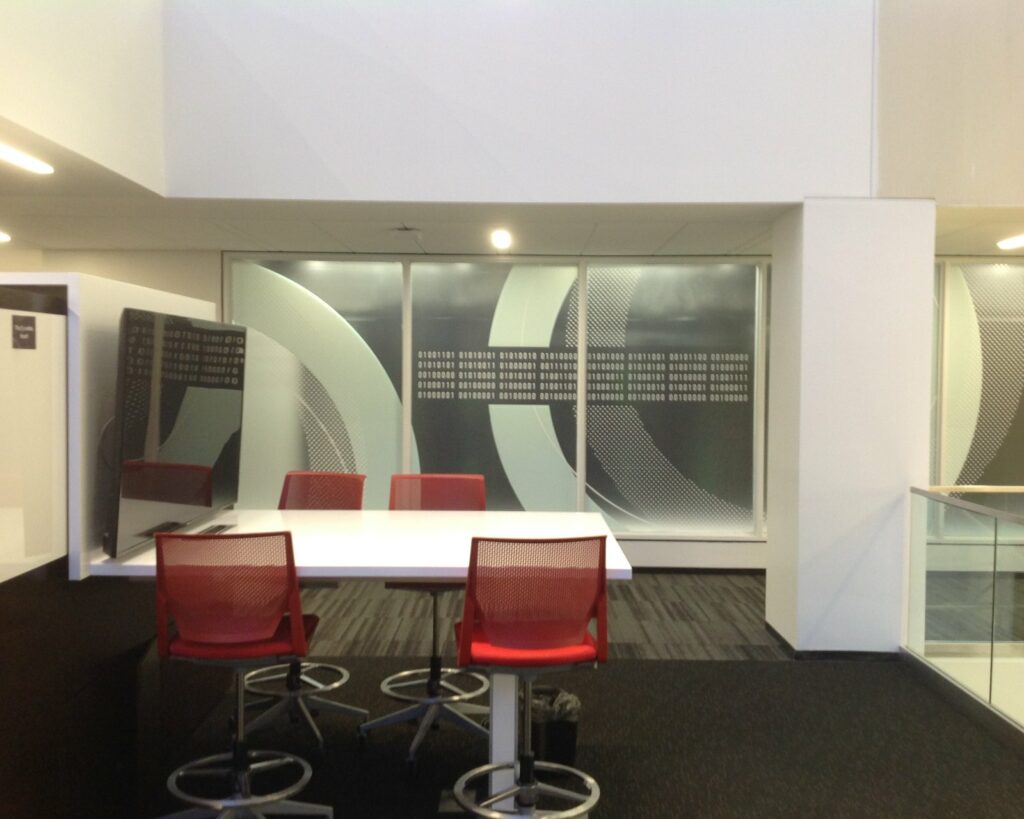 A bright modern office lobby with a glass stair rail and red stools, outfitted with interior signage by 4D SignWorx in Houston