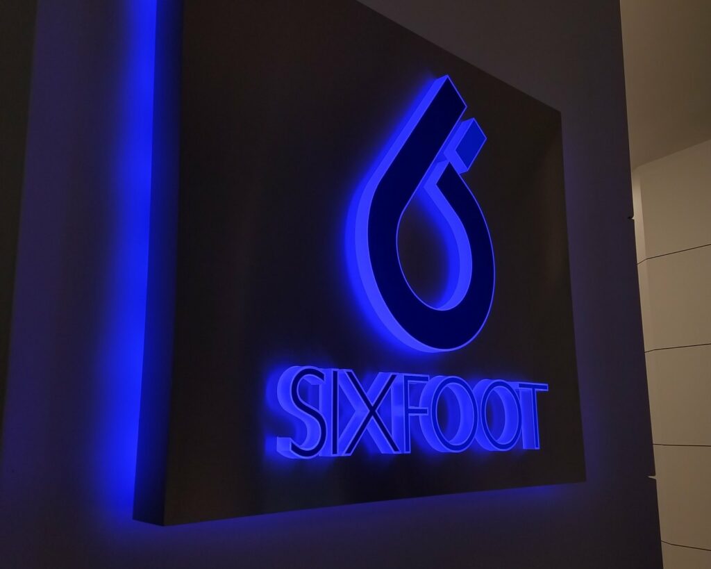 A blue halo-lit LED logo sign for Sixfoot glowing on a dark interior feature wall, built by 4D SignWorx in Houston
