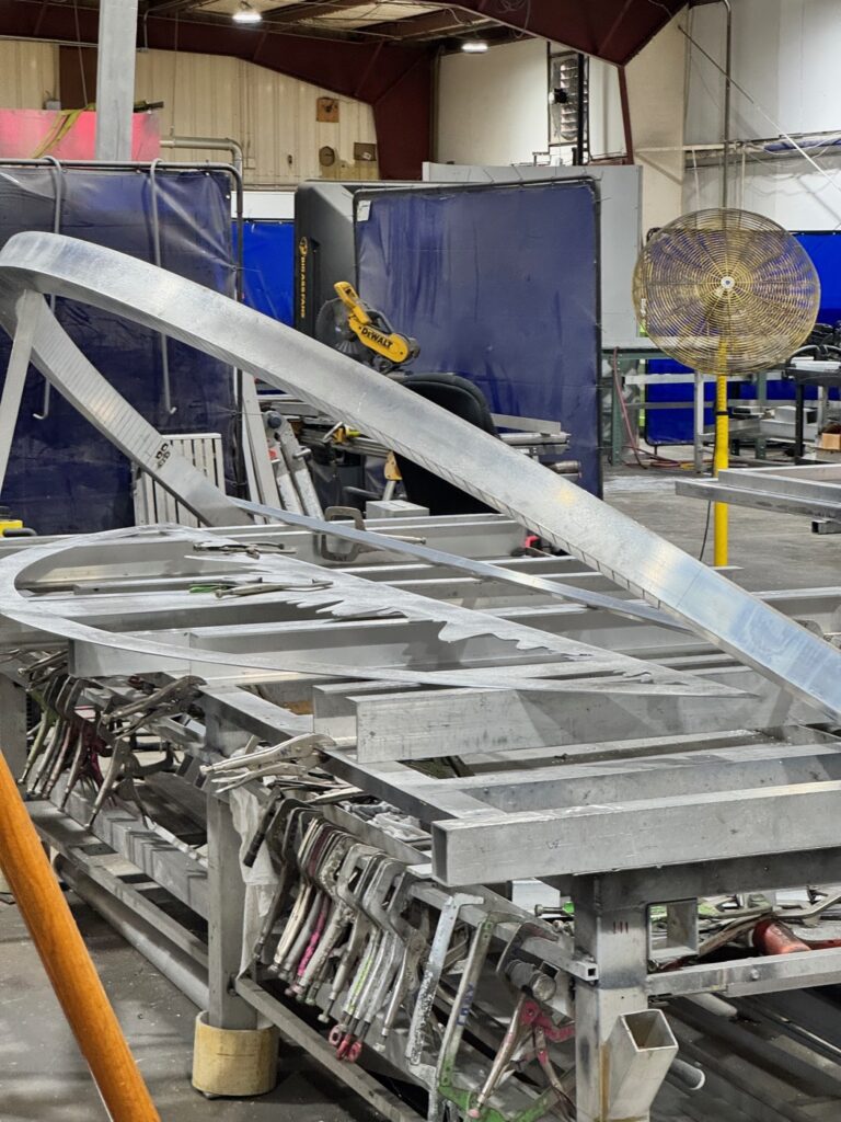 A large curved aluminum sign frame under fabrication on the 4D SignWorx shop floor